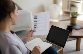 Een persoon vergelijkt vakanties op een laptop met een notitieboekje